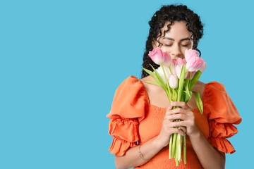 Beautiful young African-American woman with bouquet of tulips on blue background. International...