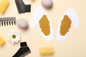 Paper bunny ears with Easter eggs, hairdressing accessories and daisy on beige background
