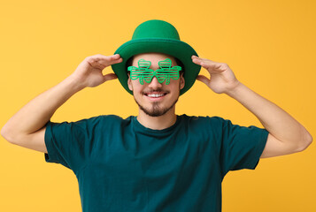 Happy young man in leprechaun's hat with party glasses on yellow background. St. Patrick's Day...
