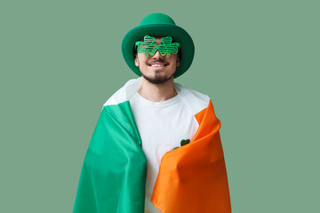 Happy young man in leprechaun's hat with party glasses and flag of Ireland on green background. St....