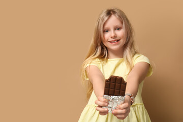 Happy little girl with sweet chocolate bar on brown background