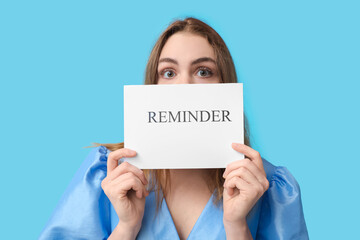 Young woman holding paper sheet with text REMINDER on blue background