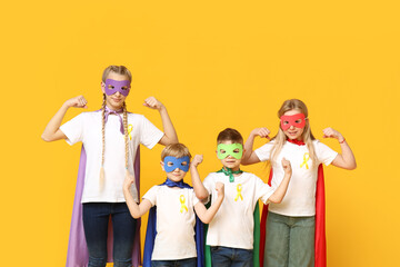 Group of kids in superhero costumes with yellow ribbons on color background. International...