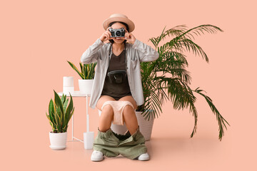 Female traveler with photo camera sitting on toilet bowl against beige background