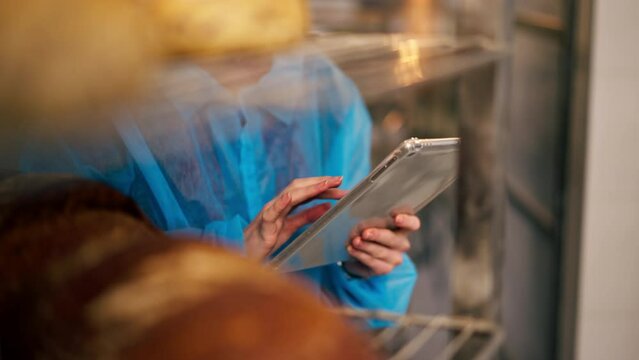 close-up in a professional kitchen young woman using a tablet creates a baking report