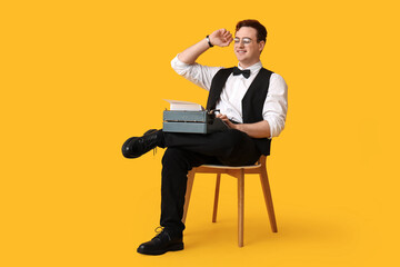 Young man with vintage typewriter on chair against yellow background