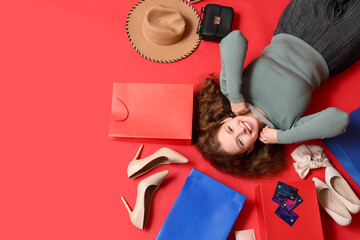 Beautiful young woman with credit cards, stylish high heels and shopping bags on red background