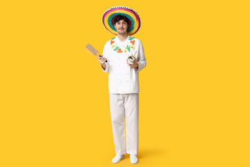 Young male chef with sombrero, painted human skull and cooking utensils on yellow background