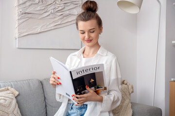 Beautiful young happy woman with magazine sitting on sofa in dressing room