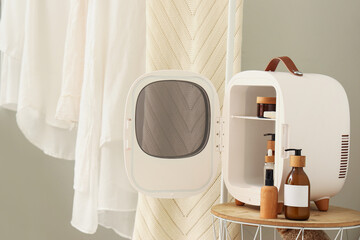 Open cosmetic refrigerator with products on table near wall in room