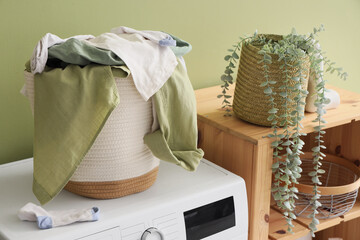 Laundry basket with dirty clothes on washing machine near green wall in room, closeup