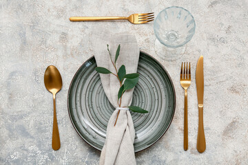 Beautiful table setting with golden cutlery and leaves on grey background