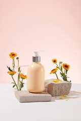 Pump bottle without label standing on a block of stone with branches of Calendula flowers. Front view. Natural cosmetic concept. Empty label for branding mockup