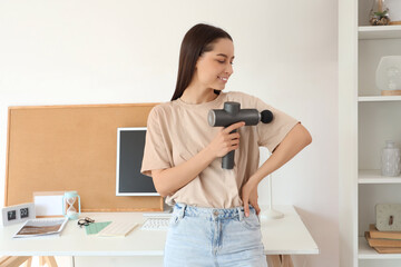 Young woman massaging her arm with percussive massager at home office