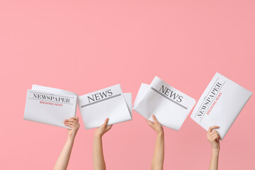 Female hands with newspapers on pink background