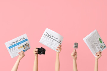 Female hands with newspapers, microphone and photo camera on pink background