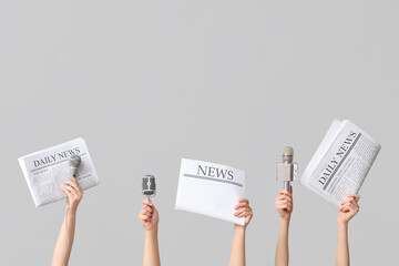 Female hands with newspapers and microphones on grey background