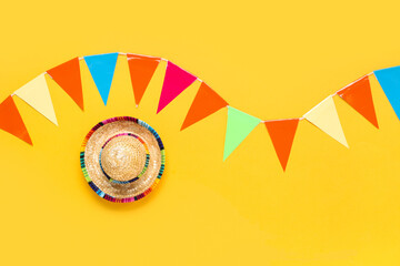 Mini sombrero and colorful flags for Festa Junina celebration on yellow background