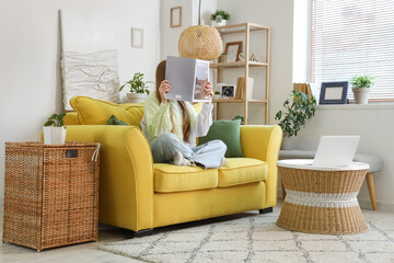 Young woman reading magazine on yellow sofa in living room