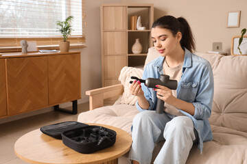Young woman with percussive massager sitting on sofa at home