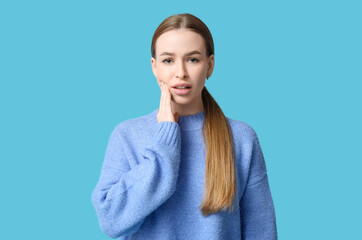 Fototapeta premium Young woman suffering from toothache on blue background
