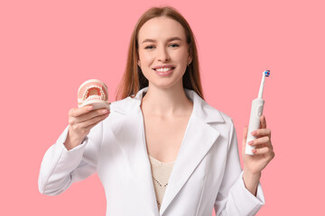 Young woman with jaw model and electric toothbrush on pink background