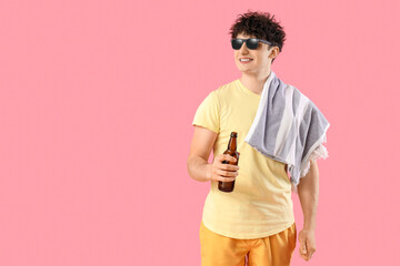 Handsome young happy man with beach towel and bottle of cold beer on pink background