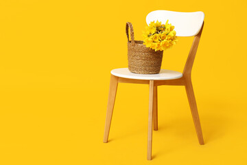 Wicker bag with bouquet of beautiful narcissus flowers on chair against yellow background