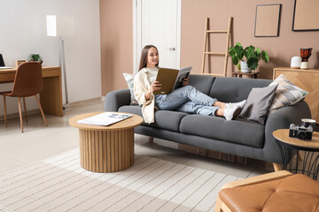 Young pretty woman reading magazine on sofa in beige living room