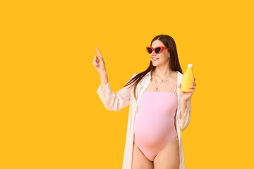 Beautiful young pregnant woman in swimsuit with bottle of sunscreen cream pointing at something on...