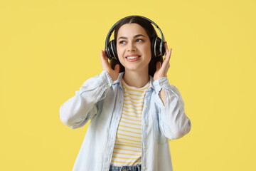 Beautiful young happy woman in headphones listening music on yellow background