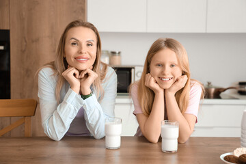 Happy mother and her daughter with cups of milk in kitchen at home