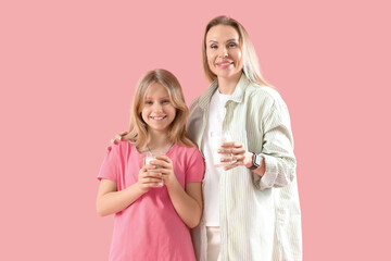 Happy mother and her daughter with cups of milk on pink background