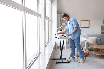 Young bearded man in headphones playing synthesizer at home
