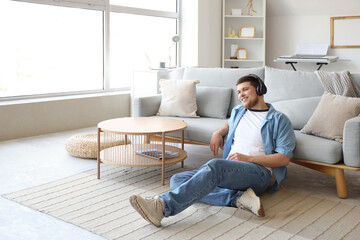 Young bearded man in headphones listening to music on floor at home
