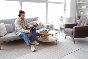 Young man in headphones with vinyl disks and record player on sofa at home