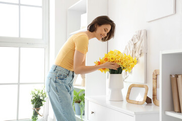 Young woman with daffodils in vase on commode at home