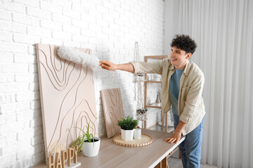 Young man cleaning painting with pp-duster at home