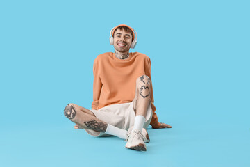 Young tattooed man in headphones listening to music on blue background