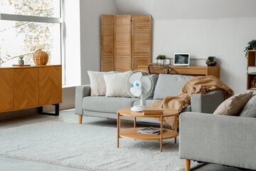 Interior of light living room with modern electric fan on coffee table