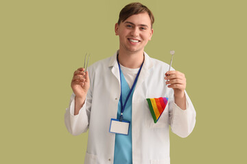 Male dentist with LGBT scarf and tools on green background