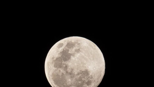 View of a full moon as it moves slowly a little upwards, showing the craters and other landforms that can be seen on the moon's face.