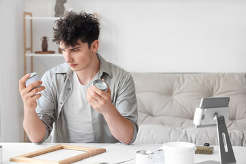 Young man with cans painting frame at home