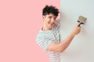 Young man with paint brush and blank poster on pink background