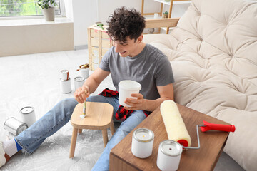 Young man with brush painting stool at home