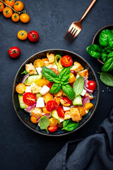 Frash vegetable salad with stale bread, tomatoes, cucumber, cheese, onion, olive oil, sea salt and green basil, black table background, top view