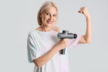 Mature woman massaging her arm with percussive massager on light background