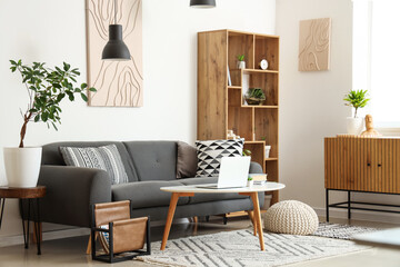 Interior of stylish living room with black sofa, coffee table, chest of drawers and shelving unit