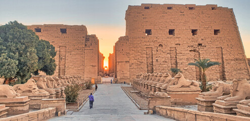 Golden glow of the rising sun rise illuminates the main axis of the Temple of Karnak with ram...