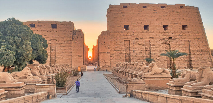 Golden glow of the rising sun rise illuminates the main axis of the Temple of Karnak with ram headed sphinxes lining the front entrance at the temple complex dedicated to God Amun-Re in Luxor,Egypt